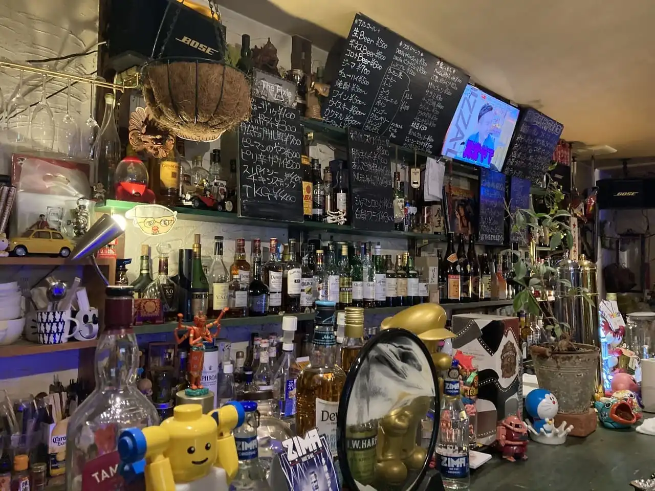 奈良市の新大宮にあるBar「@ the deep」の内観写真でカウンターの写真。黒板には白のチョークでメニューが書かれています。棚にはたくさんのお酒が並んでいます。