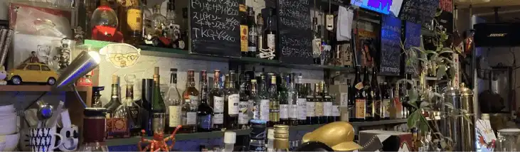 奈良市の新大宮にあるBar「@ the deep」の内観写真でカウンターの写真。黒板には白のチョークでメニューが書かれています。棚にはたくさんのお酒が並んでいます。