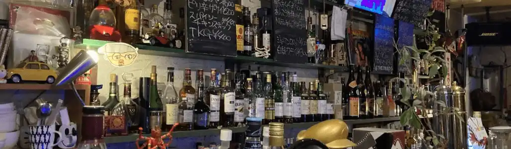 奈良市の新大宮にあるBar「@ the deep」の内観写真でカウンターの写真。黒板には白のチョークでメニューが書かれています。棚にはたくさんのお酒が並んでいます。